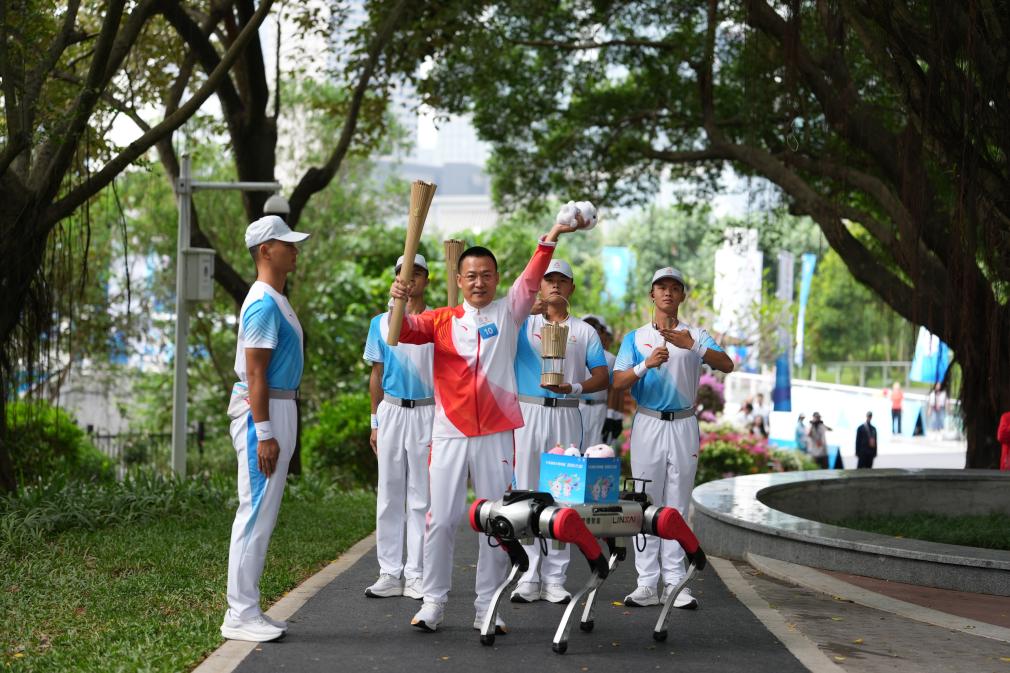 11月2日，火炬手蘭小軍（左二）在火炬傳遞深圳站展示從機器狗上取出的本屆全運會吉祥物玩偶。